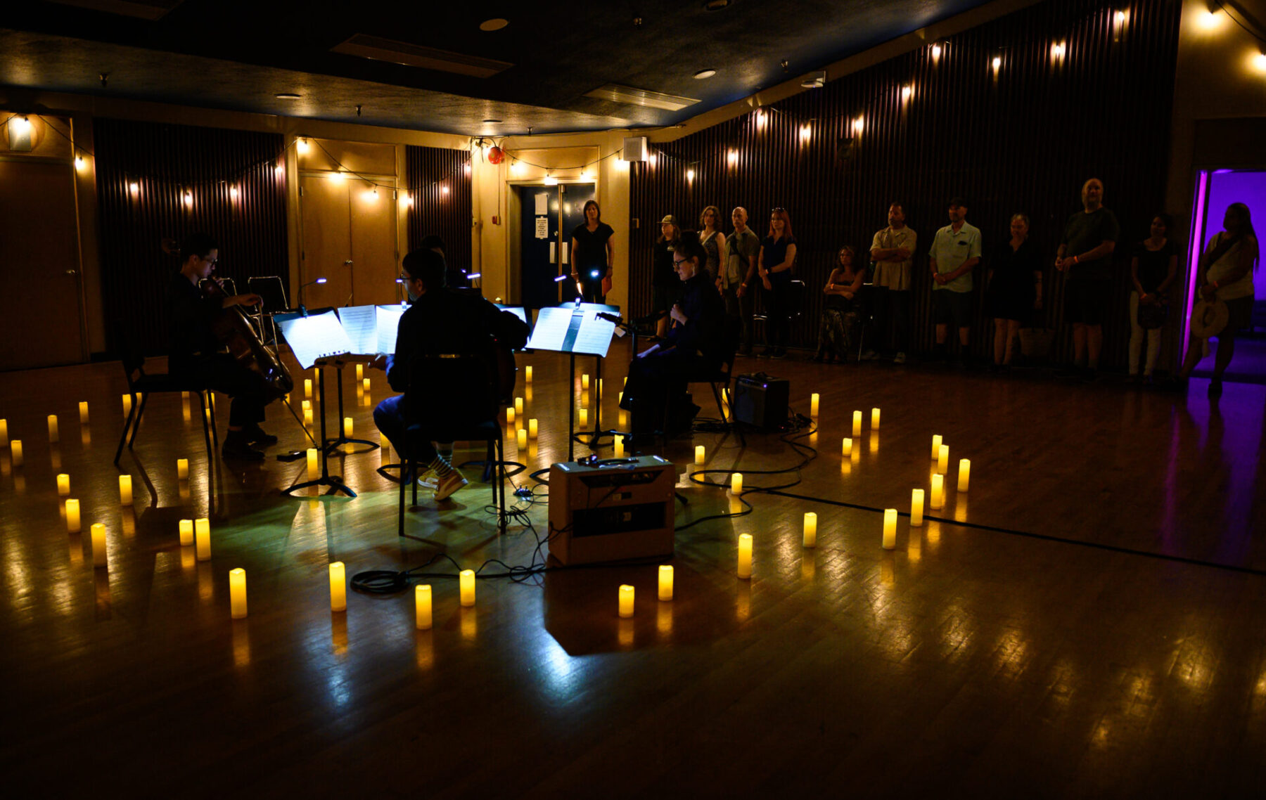 4 members of The Tempest Project Company performing in a circle of candles, in a fairly dark room.