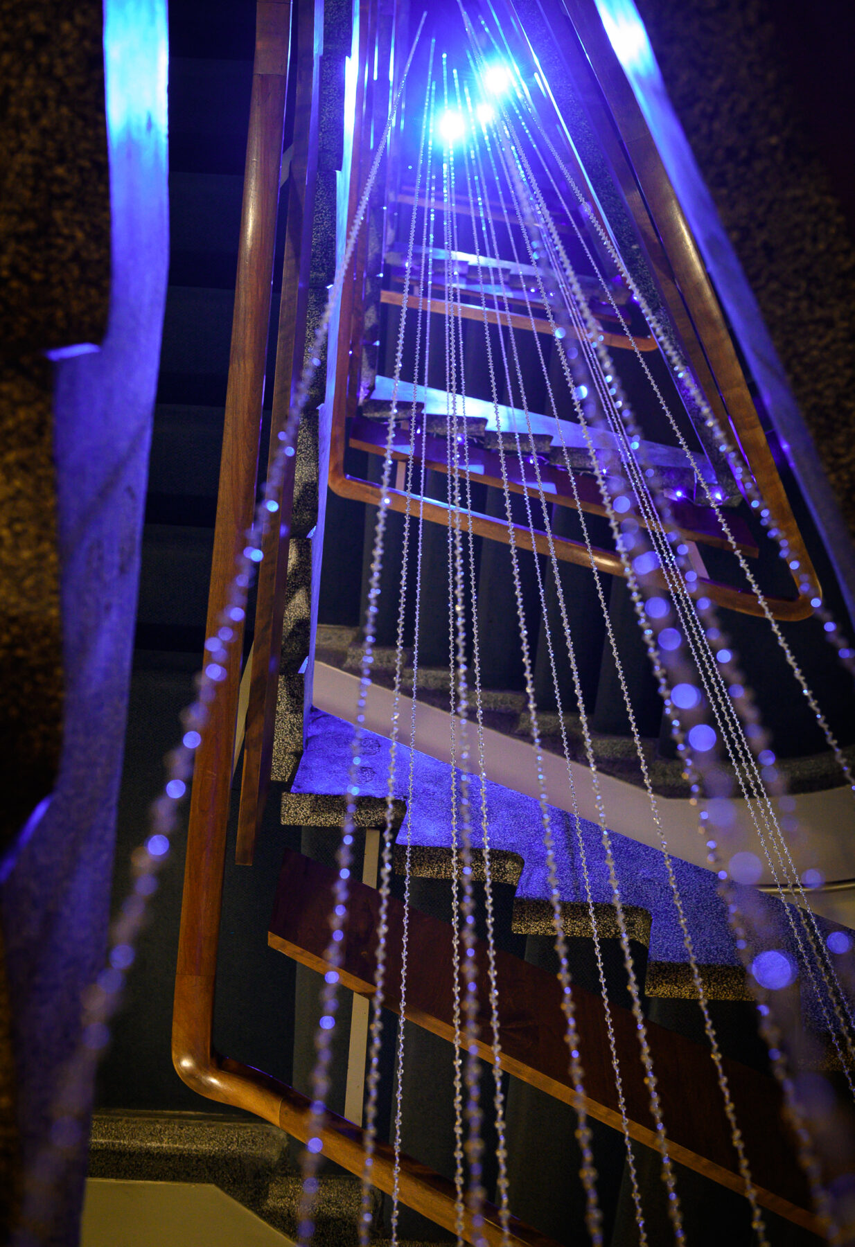 Glittery beads hanging down the centre of a stairwell with a blue light shining down.