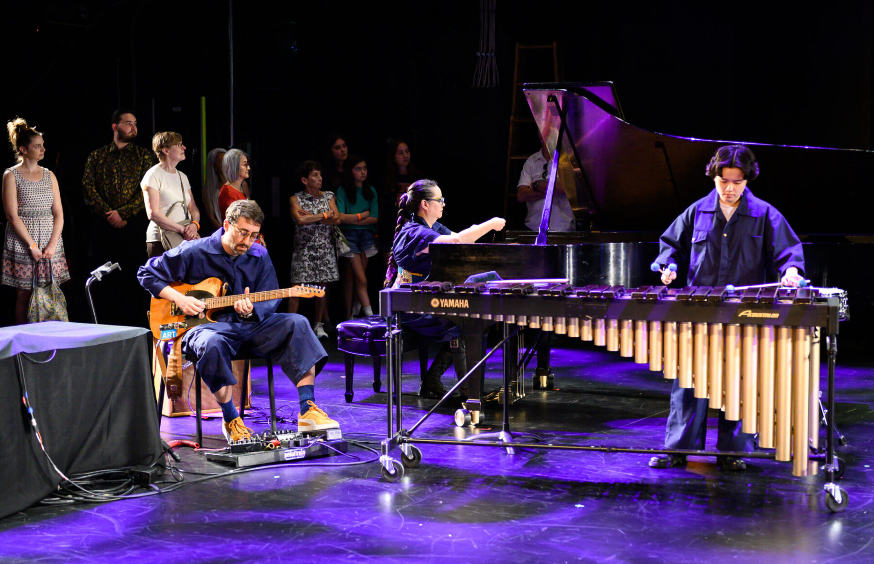 The Tempest Project Company performing on stage with audience standing behind them.