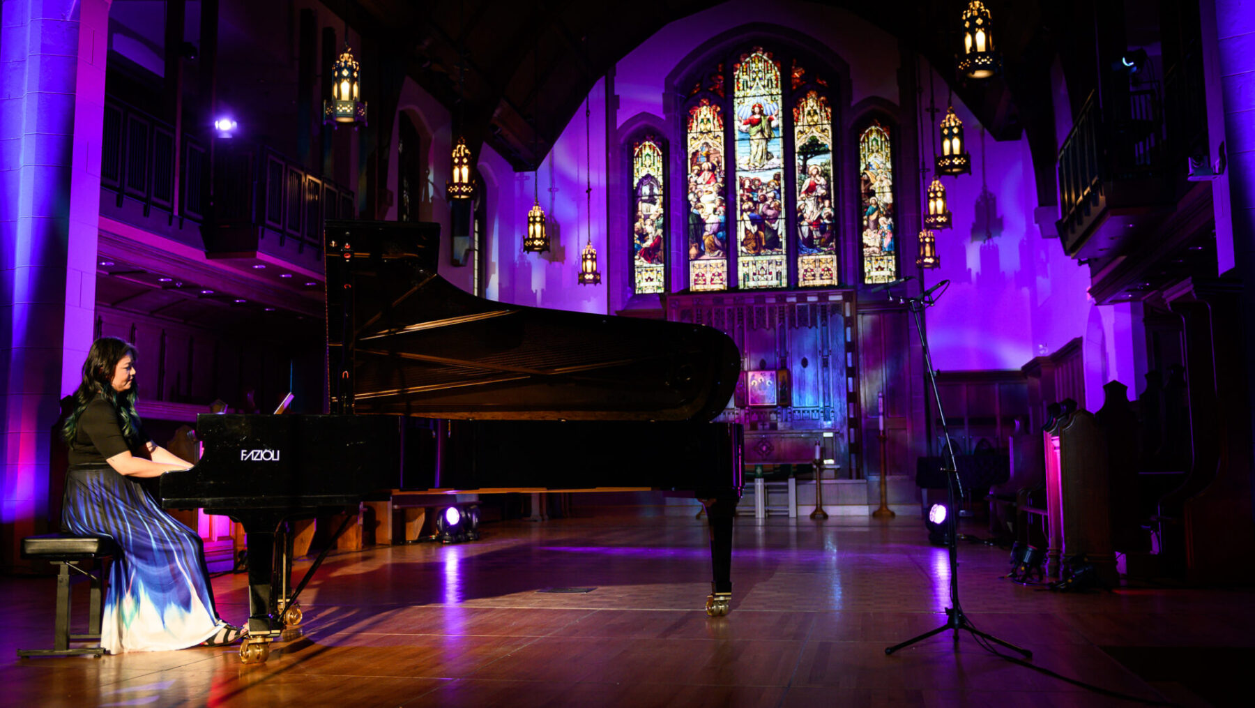 Vicky Chow sitting at a piano with the church background lit up in purple.