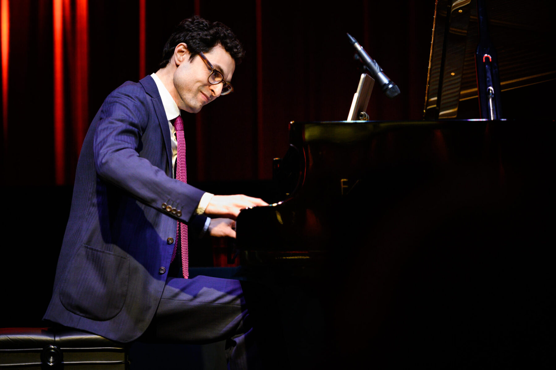 Timo Andres in a blue suit and red tie playing the piano.