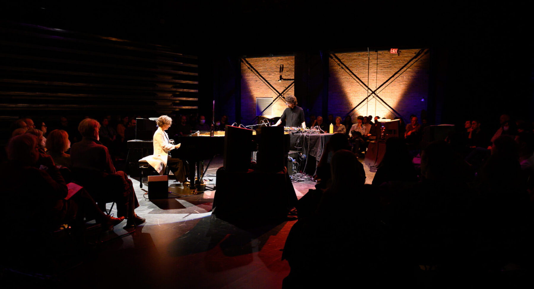 Eve Egoyan on piano and Mauricio Pauly on electronics, performing in the middle of a group of audience.