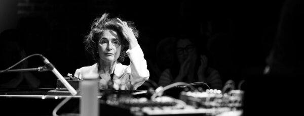 Black and white photo of Eve Egoyan at the piano with her hand resting on her head.